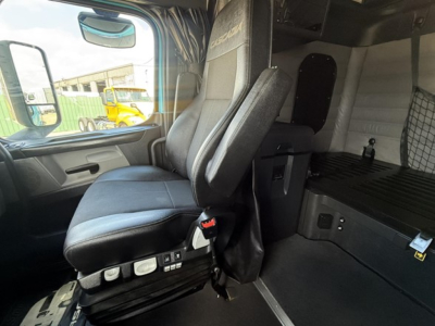 Cab interior of a Freightliner Cascadia 126 truck showing driver's seat with controls, sleeper area, and storage compartments.