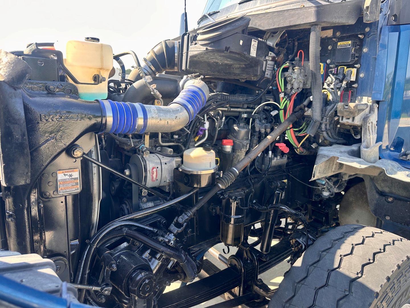 Kenworth T880 dump truck engine bay with various hoses, wiring, and fluid reservoirs visible.