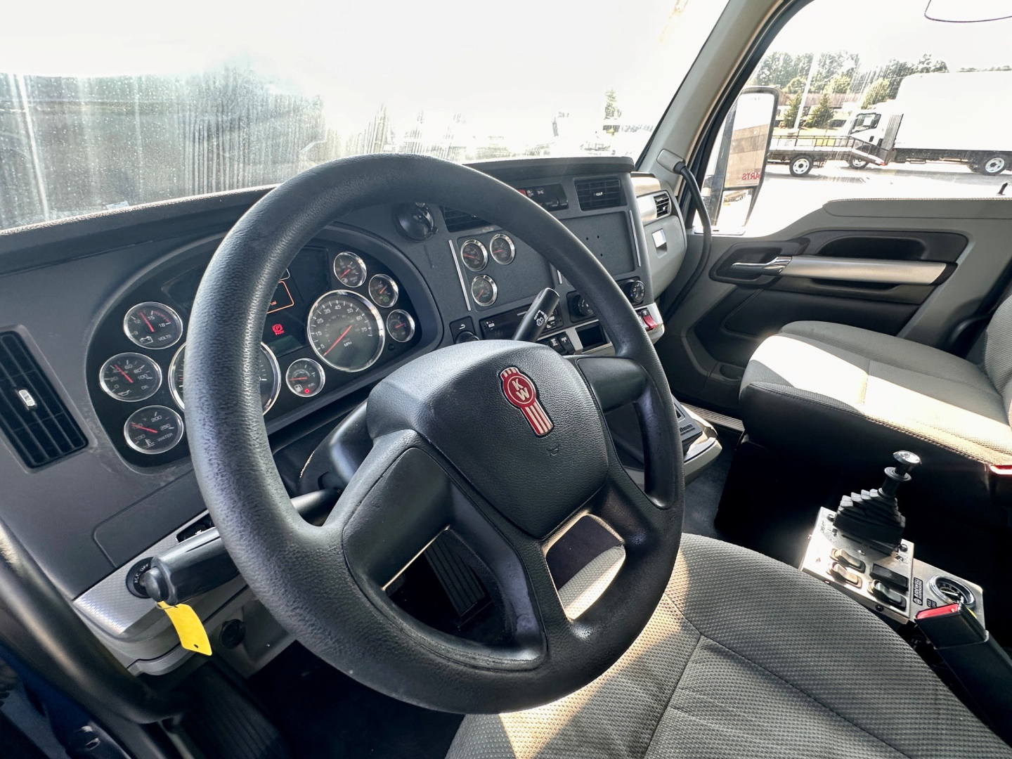Kenworth T880 cab interior showing steering wheel with Kenworth emblem, gauge cluster, center console, and gear shifter.