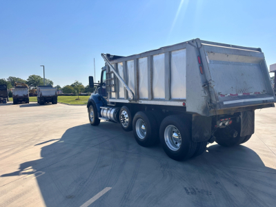 Kenworth T880 dump truck in service with aluminum dump bed, side view showing dual rear axles and side fuel tanks.
