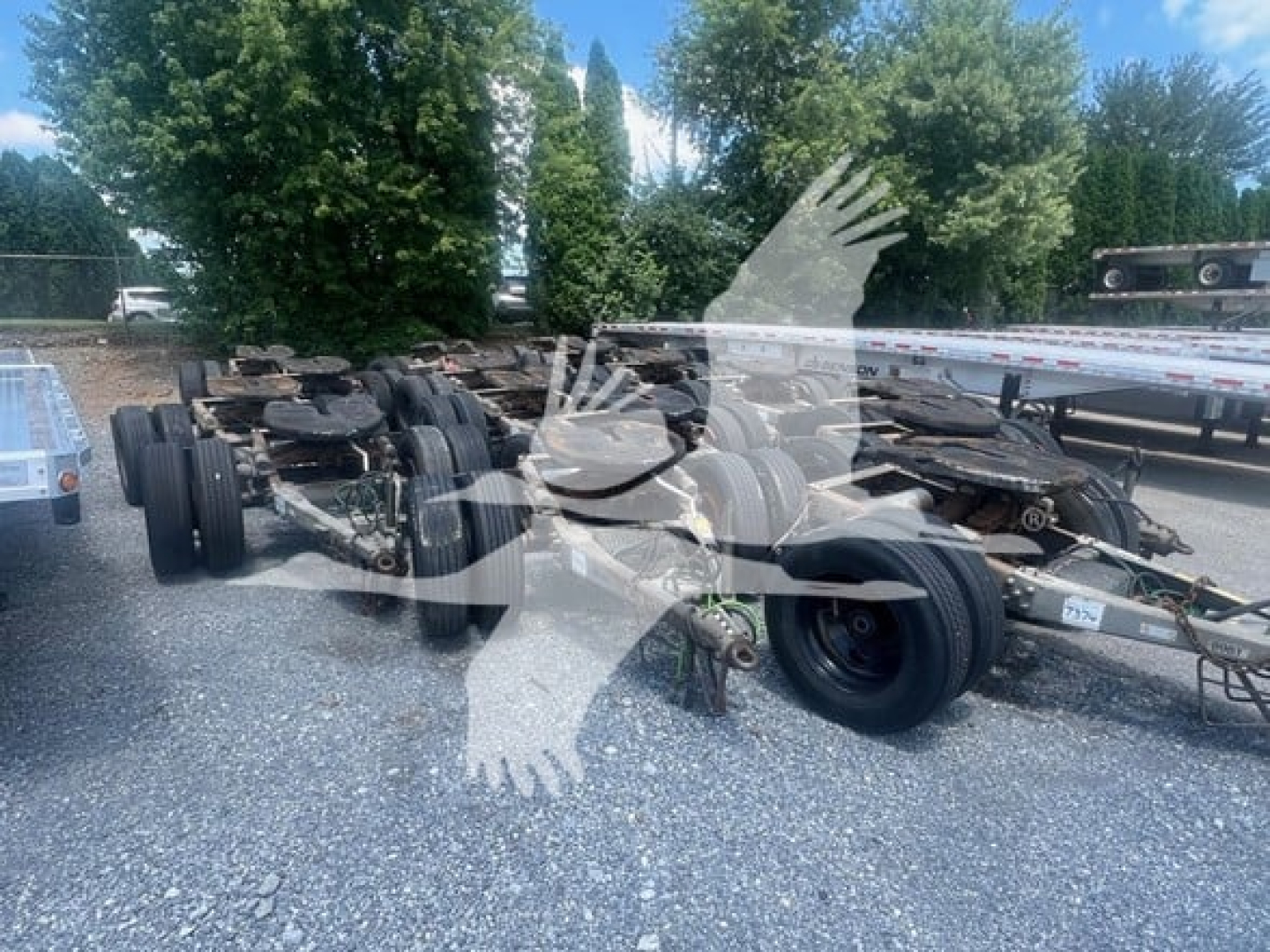 Trailer dolly chassis with multiple rear axles and tires visible; overlay watermark shapes across image.
