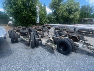 Trailer dolly chassis with multiple axles and wheels in an outdoor lot.