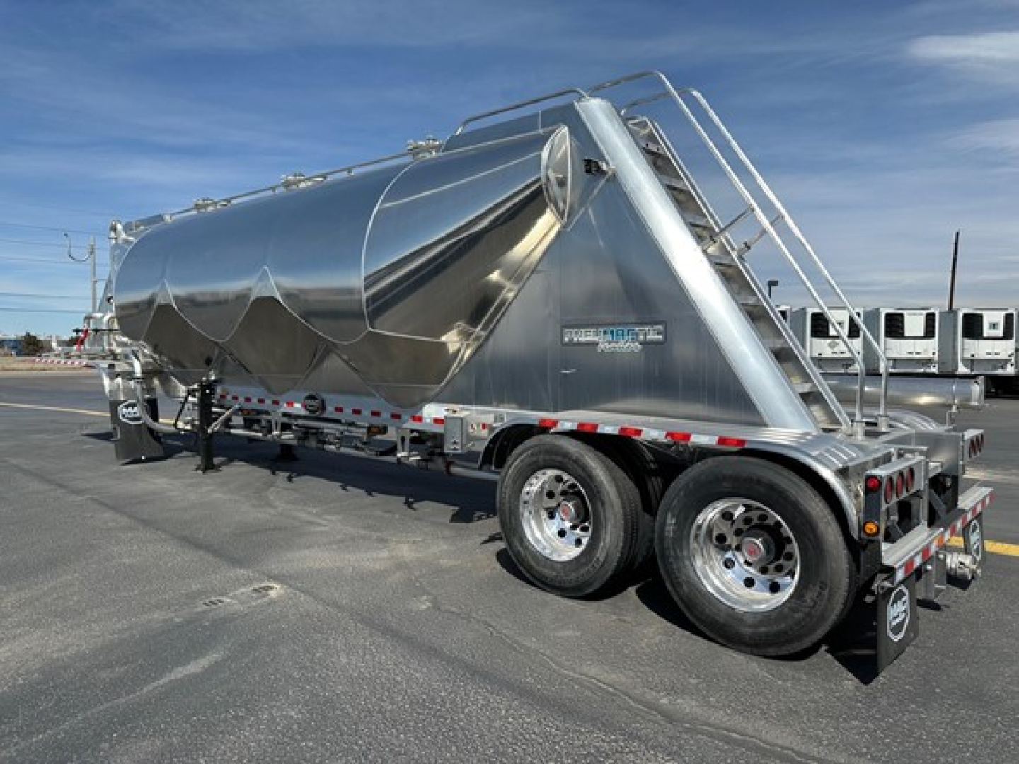 Pneumatic dry bulk trailer in polished metal with dual rear axles and ladder, side view shows 'Mac Pneumatic' label on tank.