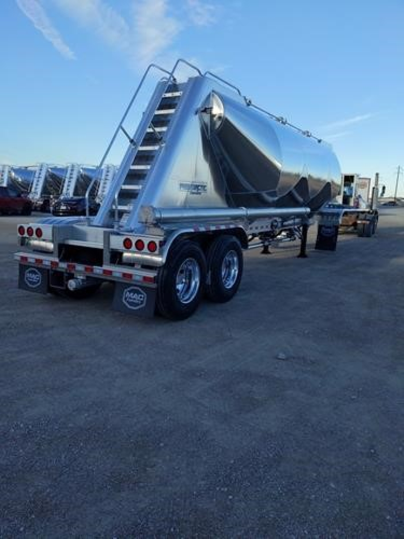 Mac Pneumatic trailer showing rear and side, aluminum hopper, dual-axle rear, stairs, and taillights. Visible text includes company logos on mudflaps and plate.
