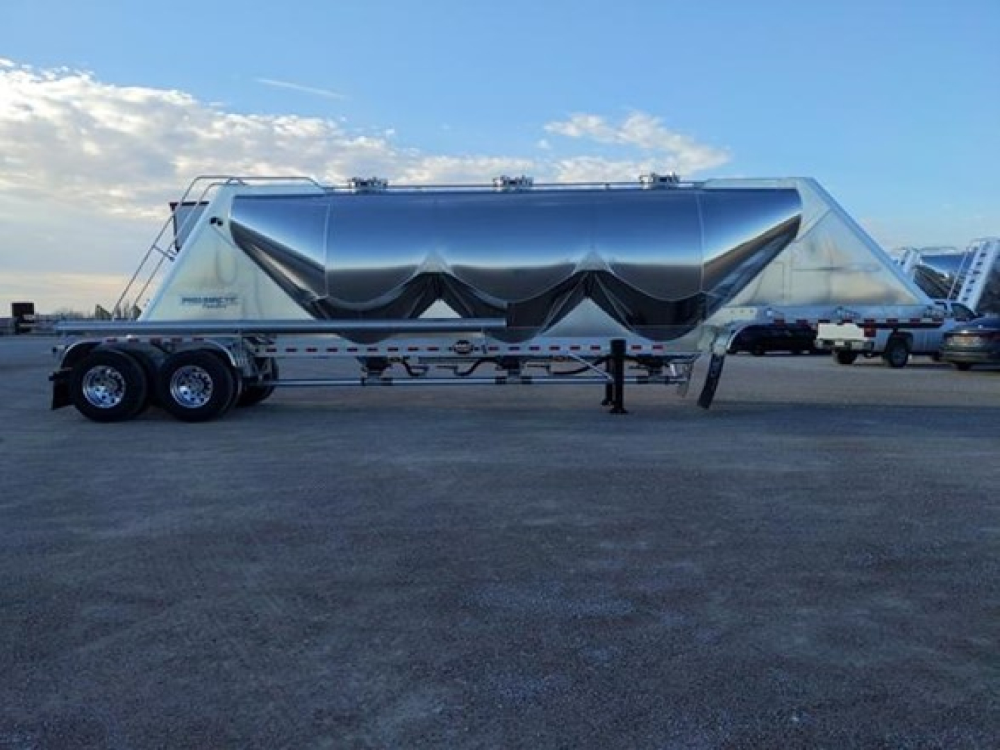 Mac Pneumatic trailer side view showing polished aluminum exterior with folding tarp system, tandem axles, and landing gear.