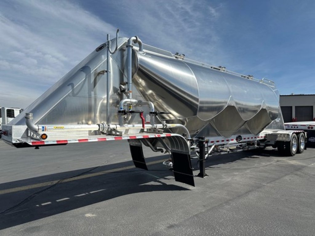 Mac Pneumatic trailer in silver showing side view with multiple hoppers, piping, and connection points; polished metal surface.