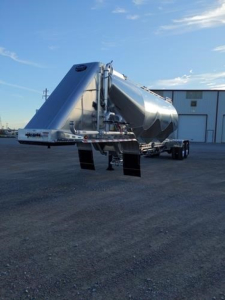  trailer showing Mac Pneumatic dry bulk trailer with polished aluminum body and rear access steps, side view, in a parking lot.