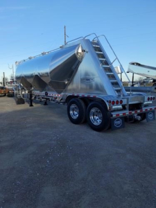 Mac Pneumatic trailer in silver metallic finish showing rear stairs and tandem axles.