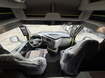Volvo VNL64T860 cab interior showing steering wheel, dashboard, two plastic-covered seats, and large front windows.