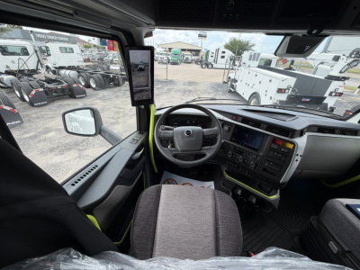 Cab interior of a Volvo VNL truck showing steering wheel, dashboard, and driver seat; left mirror, side window, and multiple control screens visible.