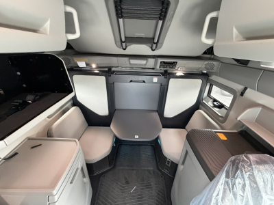 Cab interior of a 2027 Volvo VNL64T860 sleeper showing front seating area, table, overhead storage, and side compartments.