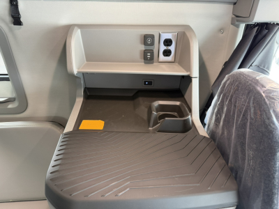 Volvo VNL64T860 truck interior showing entry area with a small upper latch panel, power outlets, sandy beige accents, and a textured rubber floor mat.