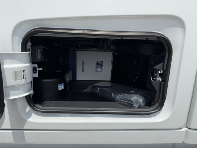 Trunk/storage compartment of a Volvo truck showing a white box labeled XANTREX and a black cylindrical component; spare parts in storage area.