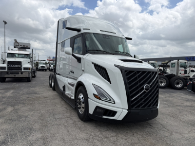 Volvo VNL64T860 conventional sleeper truck in white, front-left view showing grille, headlights, and aerodynamic cab; dealership lot in background.