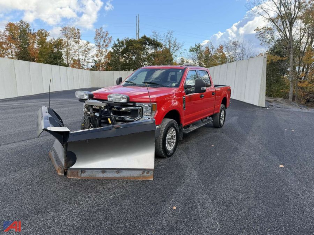 Ford F-250 Super Duty pickup with large V-plow attached, red crew cab, cargo bed, in an outdoor lot.