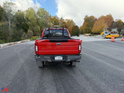 Ford F-250 rear view with a red V-Plow, tailgate badge, and rear bumper; highway construction cones in background.