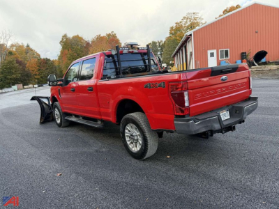 Ford F-250 Super Duty pickup with V-Plow in red, rear and left side view, four-wheel drive badge, tow hitch, numeric plate area, showroom lot.