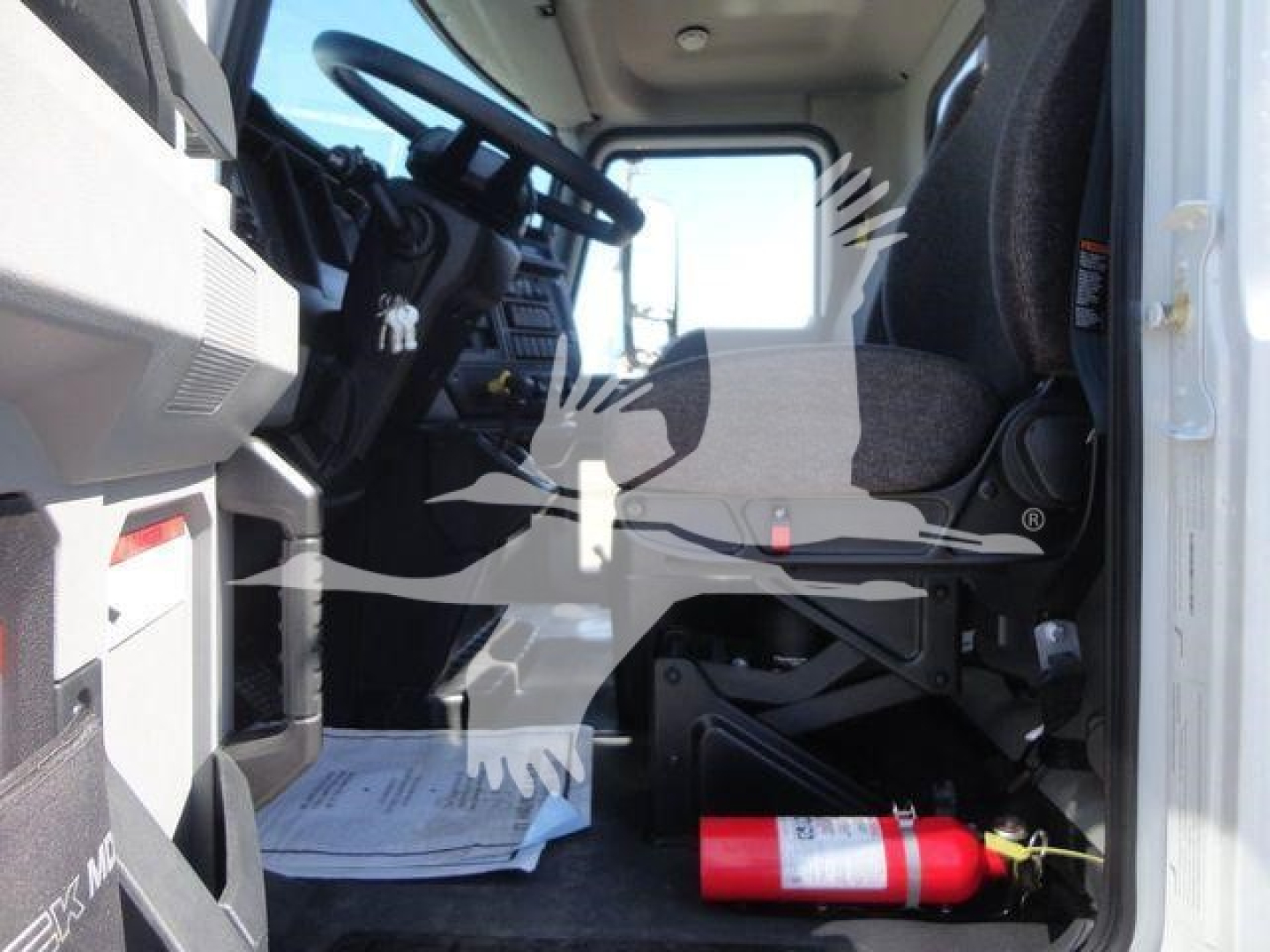 Cab interior of a 2027 Mack MD6 truck showing steering wheel, dashboard, driver's seat, and a red fire extinguisher on the floor near the door.