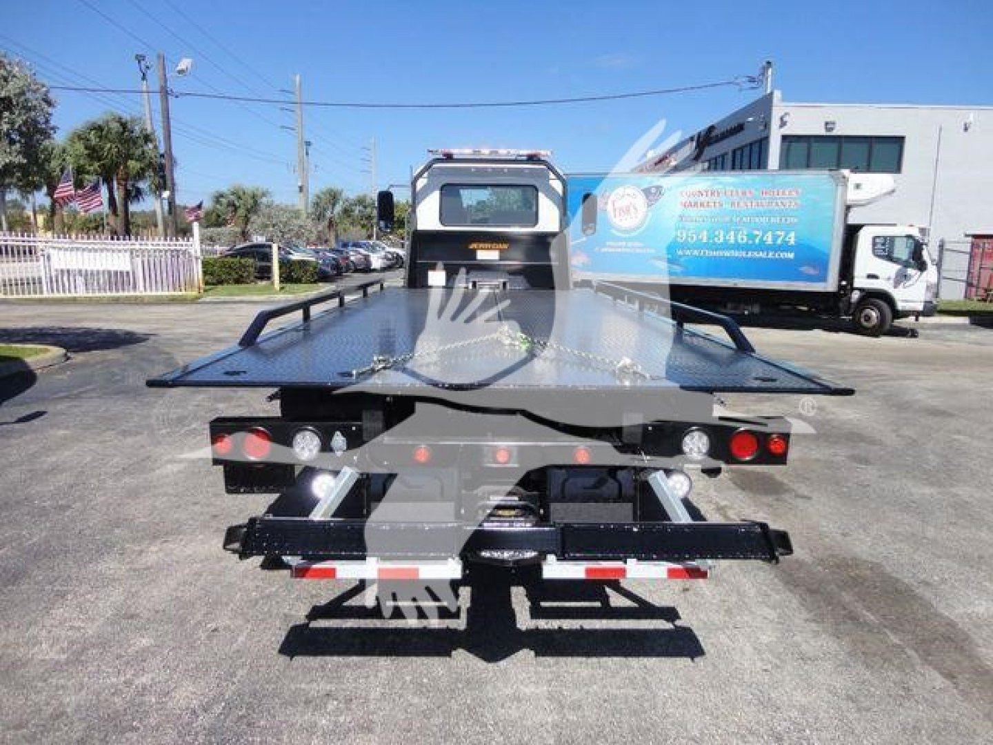 Flatbed tow truck platform shown from rear with lights and hydraulic bed rails, MD6 roll-back truck on a dealership lot.