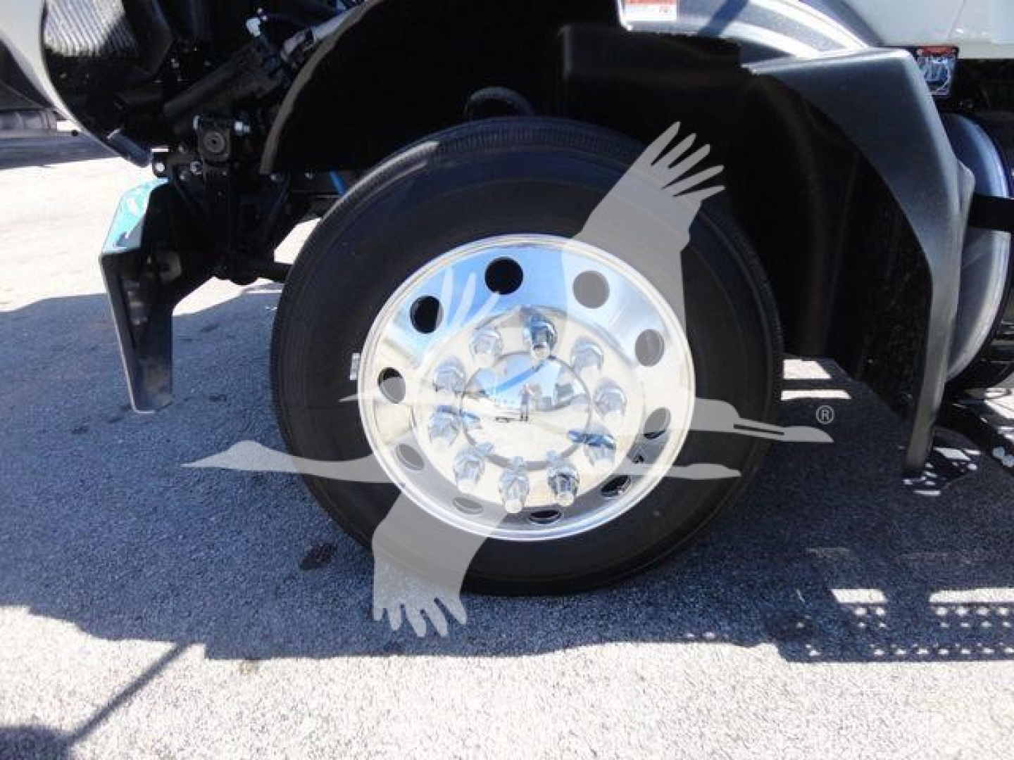 Front wheel and fender of a new 2027 Mack MD6 rollback truck showing steel hub and tire, partial chassis components.
