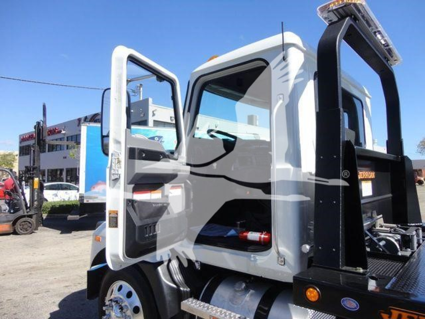 Mack MD6 rollback truck cab view showing open door and operator compartment with steps, hydraulic equipment, and metal frame.