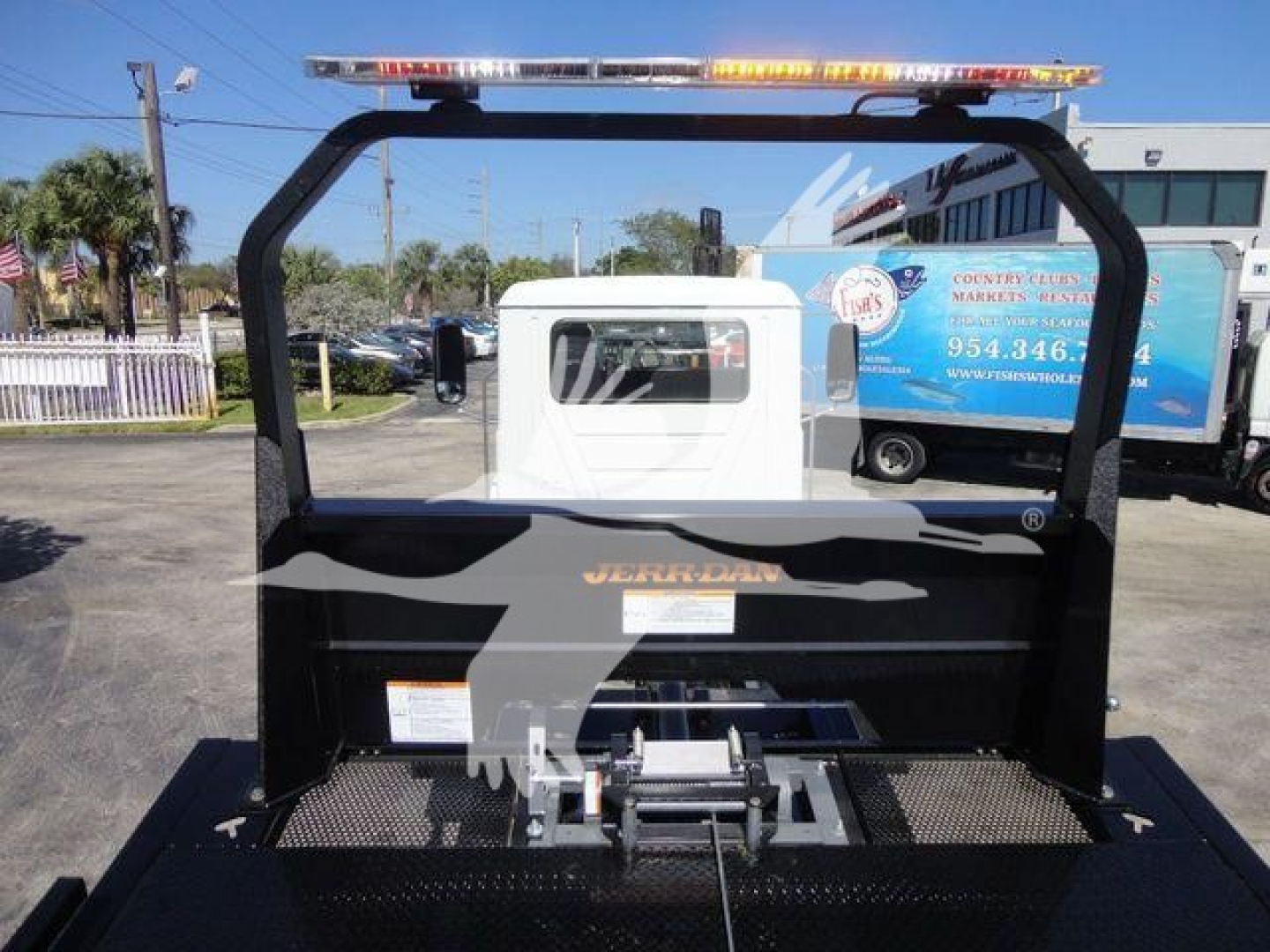 Truck bed with a hoist and rollover device in a Mack MD6 pickup; rear view showing orange warning bar on top and equipment rack.