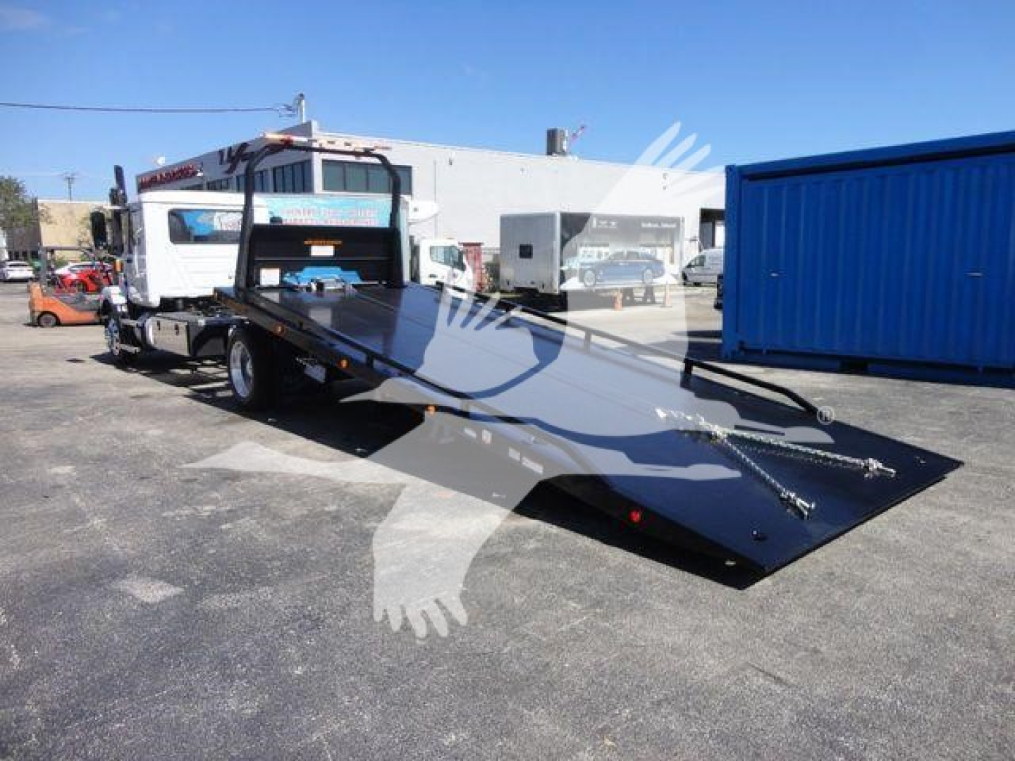 Truck with flatbed rollback showing ramped tow bed and Mack MD6 cab in background.