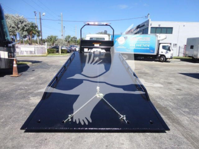 Truck bed view of a 2027 Mack MD6 rollback bed with black glossy surface and chain anchors, front cab visible in background.