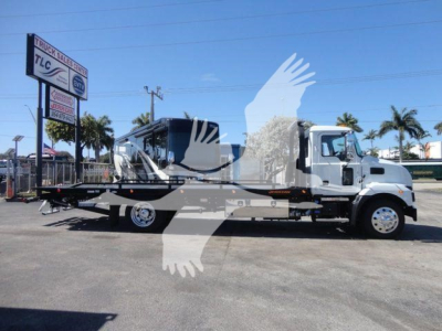 New 2027 Mack MD6 rollback truck in a lot, flatbed behind cab, dealership sign in background.