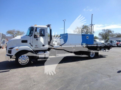 Truck cab and flatbed rollback with blue container on a lot; clear sky.