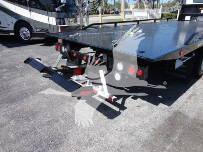 Flatbed tow truck with a metal diamond plate platform and rear equipment, hitch assembly, and taillights visible.