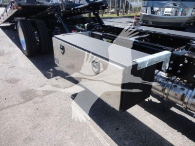 Truck chassis side view showing a rectangular metal toolbox mounted under the cab of a Mack MD6 rollback truck.