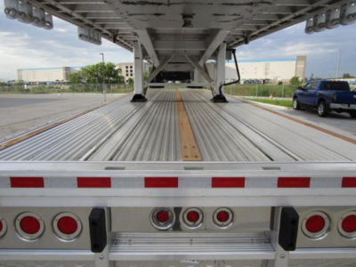 Flatbed trailer bed interior with metal decking and a centered wooden plank, rear lights and frame visible.