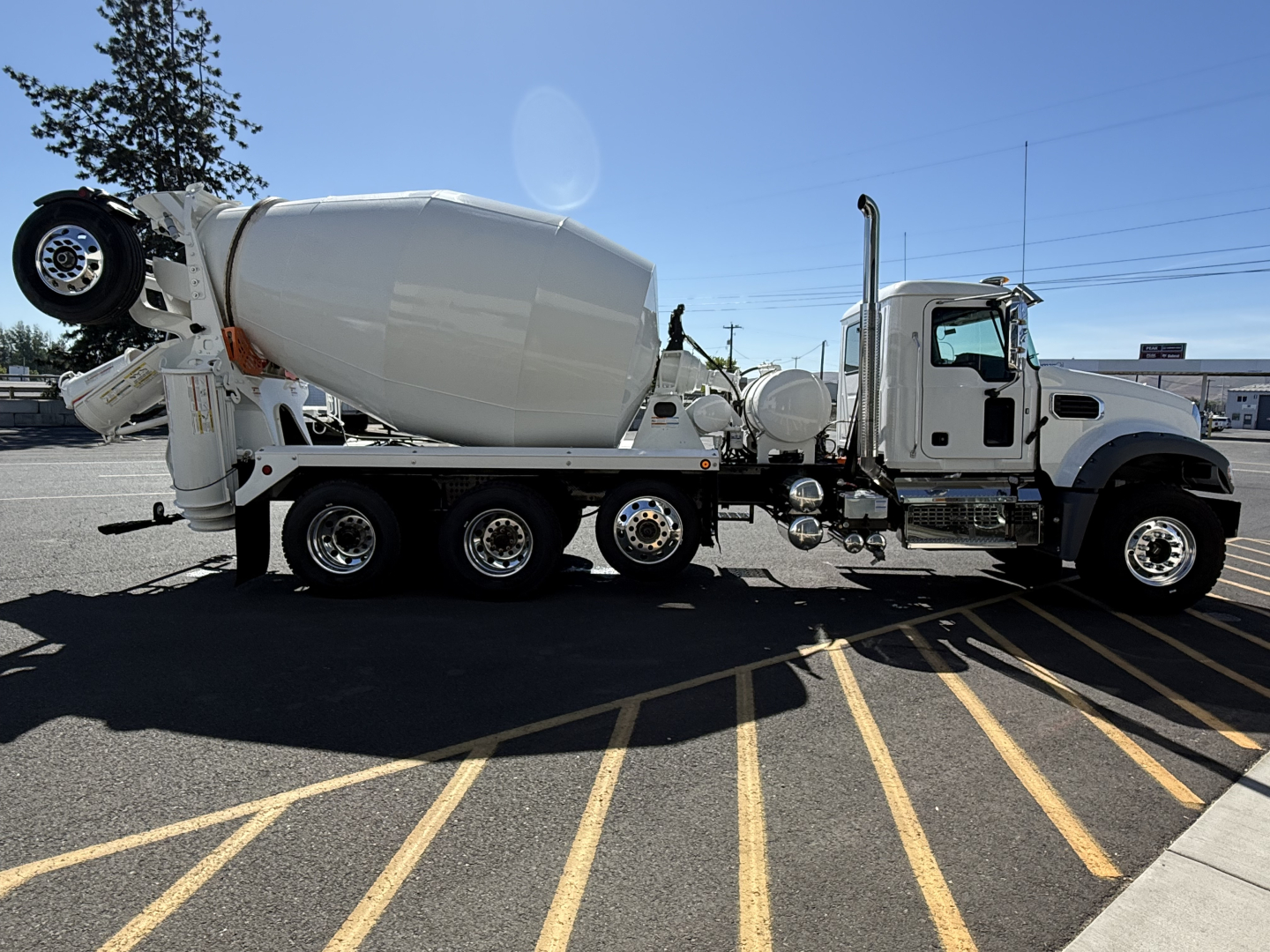 Concrete mixer truck with white cab and drum, side view showing cement mixer apparatus, spare tire mounted near rear, multiple axles.