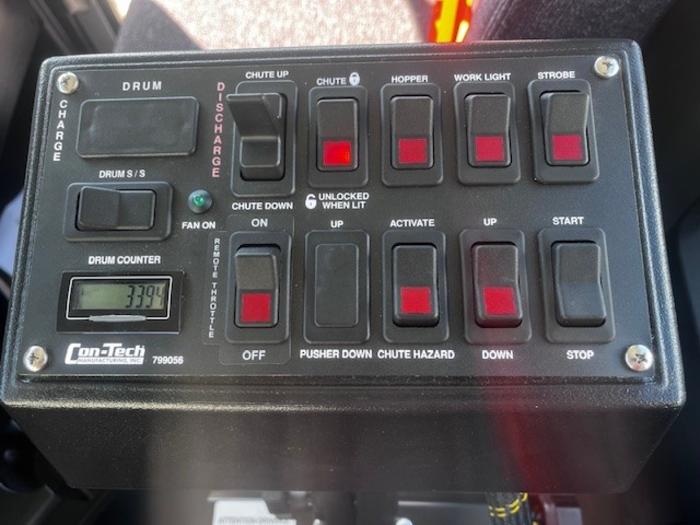 Control panel of Mack mixer truck with labeled switches and a small display reading '1339' or similar; includes labels DRUM, CHARGE, CHUTE UP, CHUTE DOWN, HOPPER, WORK LIGHT, STROBE, FAN ON, UP, START, STOP, OFF, ON, DOWN, CHUTE HAZARD, PUS