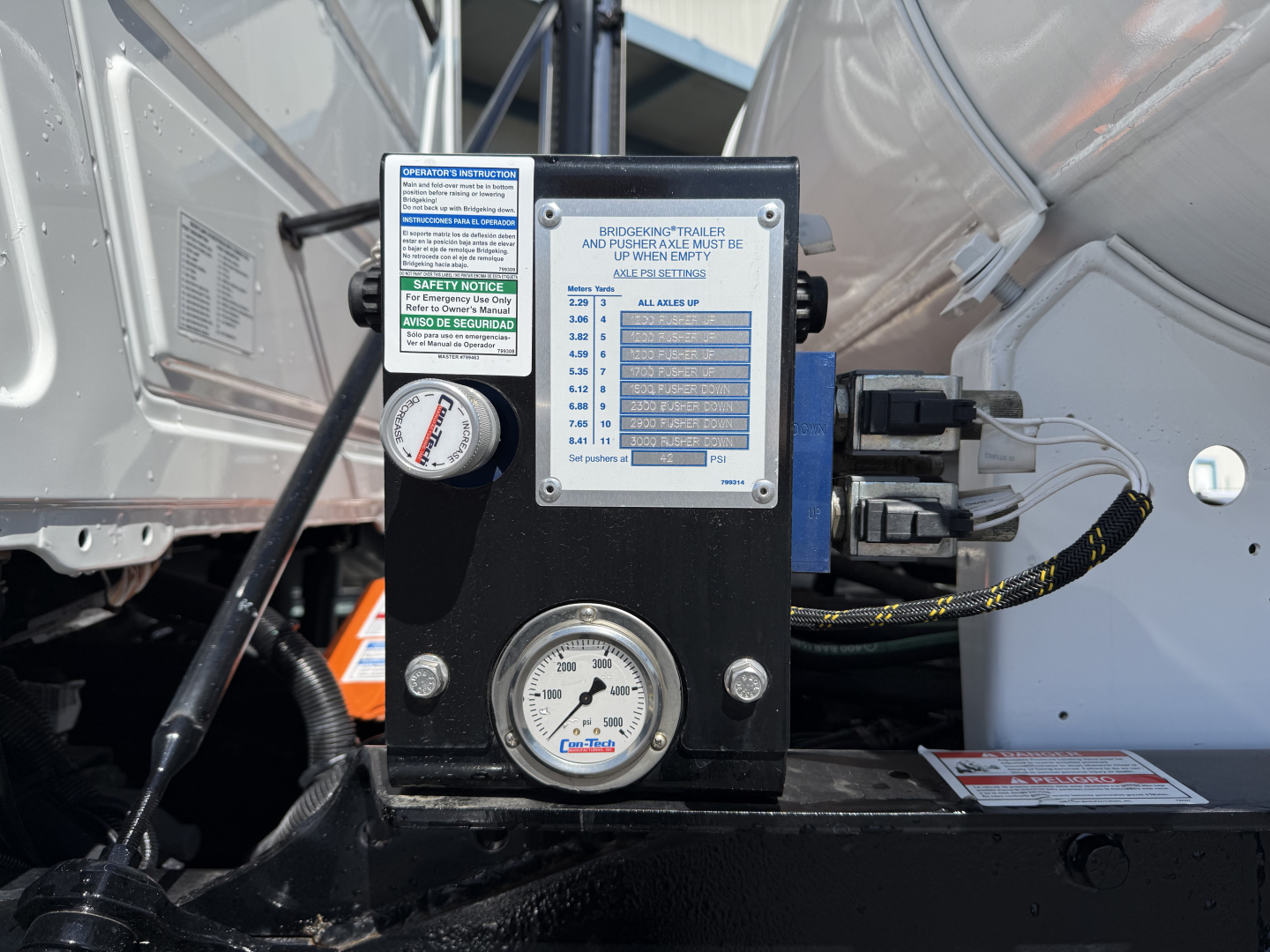 Mack mixer truck engine bay with control panel showing gauges and labels, including a pressure gauge and warning placard.