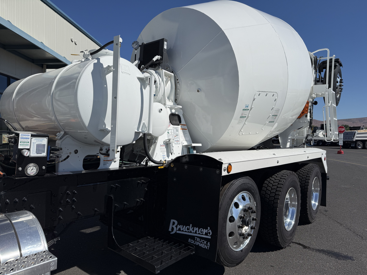 Mixer truck on trailer showing large white cement mixer drum and chassis with three axles and chrome wheels; visible controls and equipment mountings on the side.