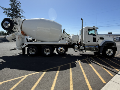 Concrete mixer truck with white cab and drum, side view showing cement mixer apparatus, spare tire mounted near rear, multiple axles.