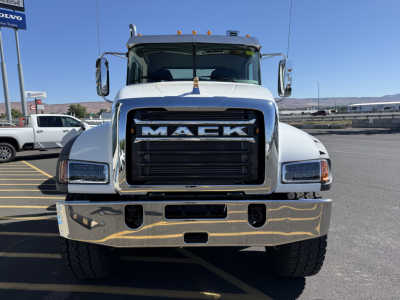 Mack truck front view showing bold grille with MACK logo and chrome bumper, side mirrors, headlights, and cab; clear blue sky.