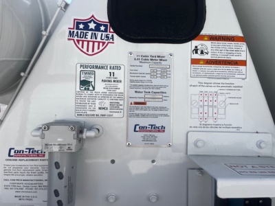Mixer truck rear with labels: Made in USA badge, performance rating 11, Con-Tech/mixer manufacturer plate, warning and instruction diagrams, water tank capacity chart.