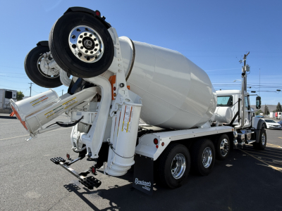 Mixer truck rear view showing cement mixer drum and ramps, three rear axles, dual rear wheels, chassis and hydraulic components visible.