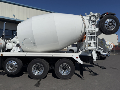 Mixer truck side view showing white cement mixer drum, rear ladder, spare wheel, and dual rear axles with chrome rims.
