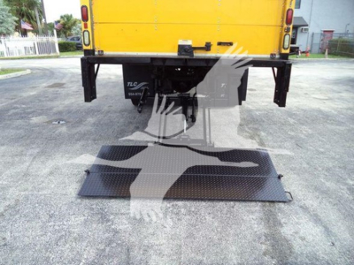 Rear view of a yellow 2018 International Durastar 4300 box truck with a lowered black metal ramp/stairs attached to the back, showing bumper and hitch area.