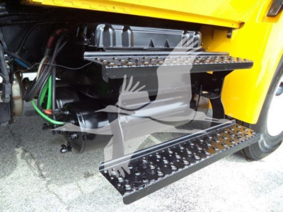 Truck runner's under-step with metal steps and hydraulic lines visible in engine bay area of a yellow International Durastar 4300.