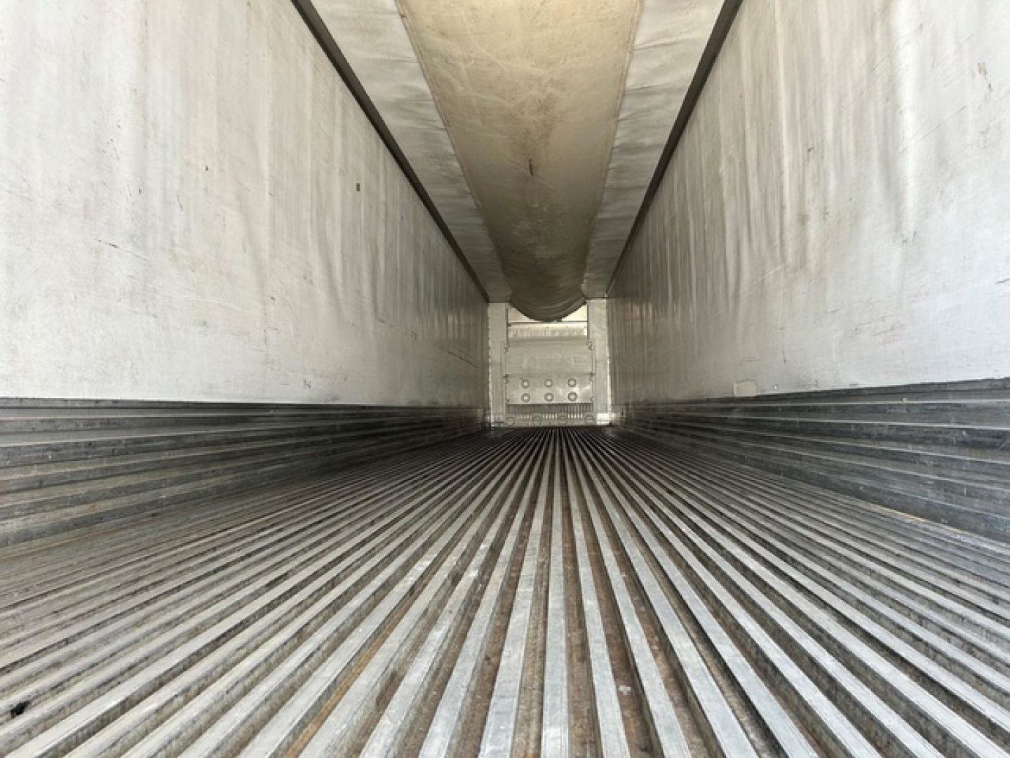 Reefer trailer interior showing ribbed flooring and side walls with ceiling heat duct, empty cargo space.