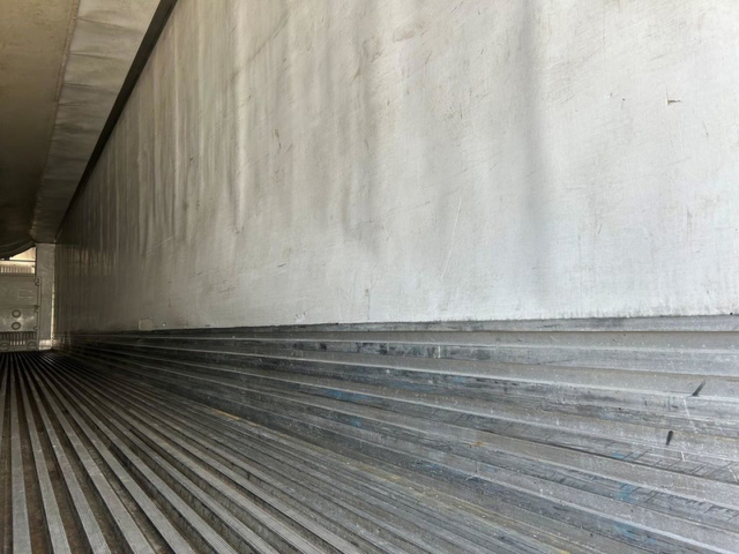 Trailer interior wall with ribbed metal flooring and sidewall in a refrigerated trailer showing corrugated lower wall surface.