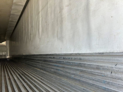 Trailer interior wall with ribbed metal flooring and sidewall in a refrigerated trailer showing corrugated lower wall surface.