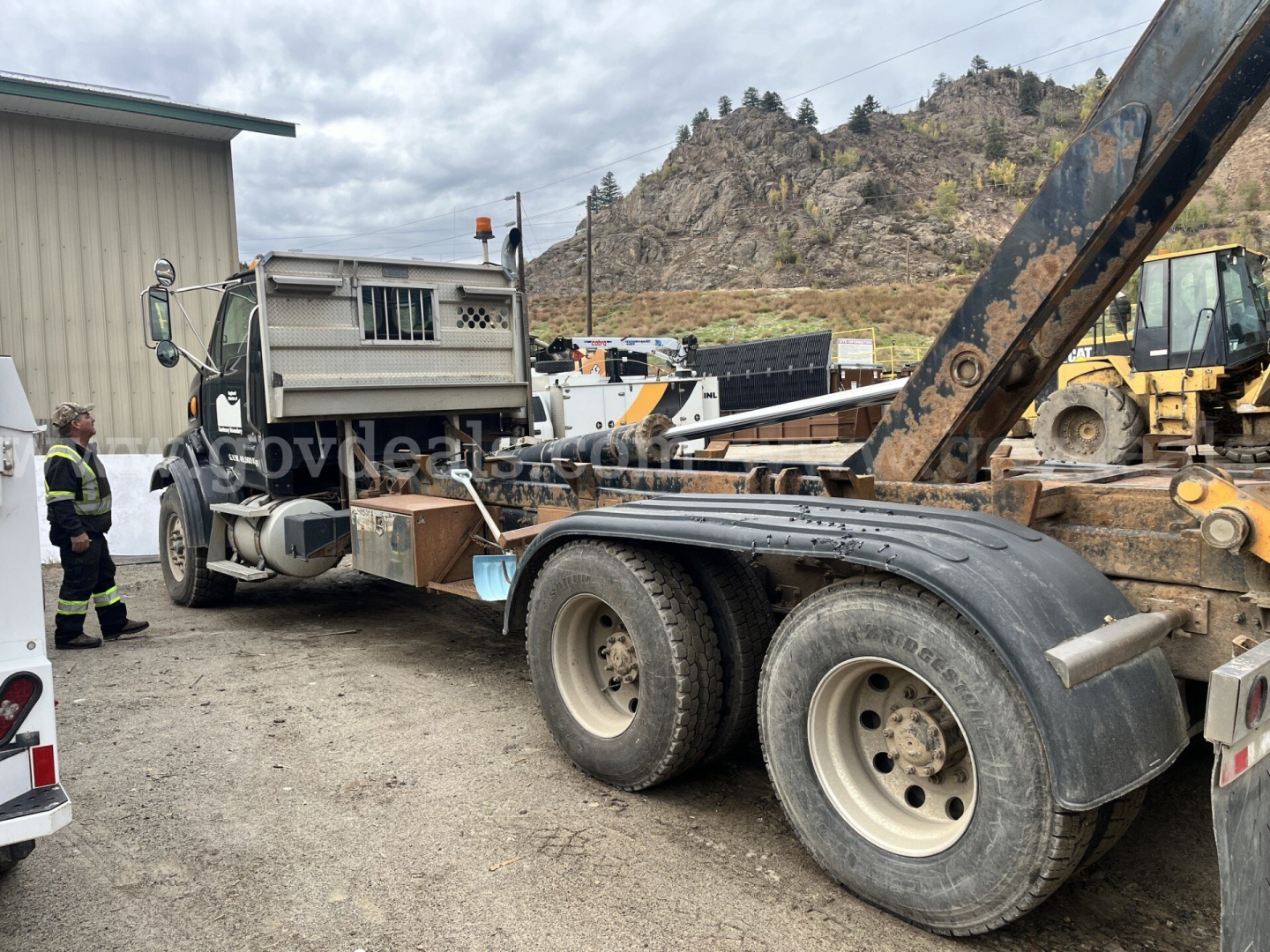 2007 Sterling LT9500 roll-off truck chassis with rear dual tires and hydraulic arm; visible labels include stock/construction equipment markings and a warehouse backdrop.