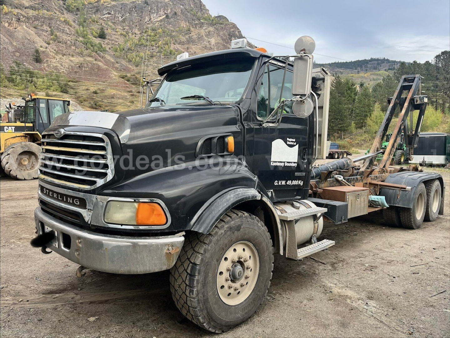 Sterling LT9500 roll-off truck in-service showing front grille, cab, and attached loading chassis with hydraulic arm and debris bed, black paint, visible tires.