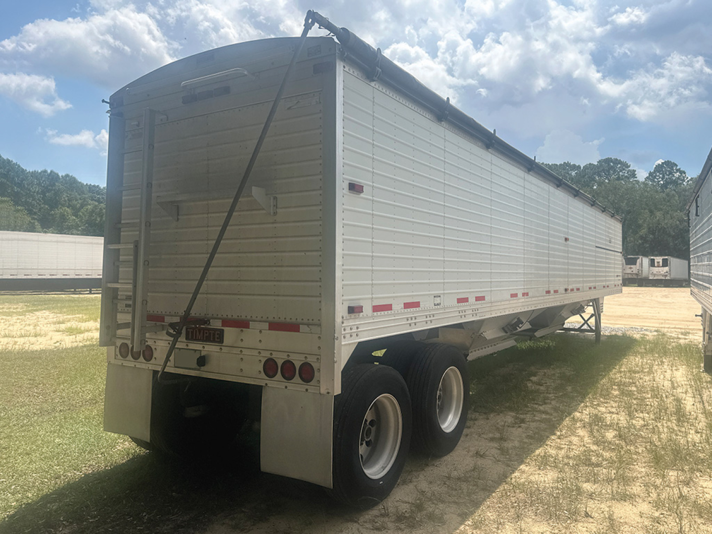 Trailer showing side and rear view of a 2022 Timpte Super Hopper with aluminum sides, dual rear axles, and raised steel landing legs.